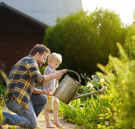 Middle,Age,Man,And,His,Little,Son,Watering,Flowers,In